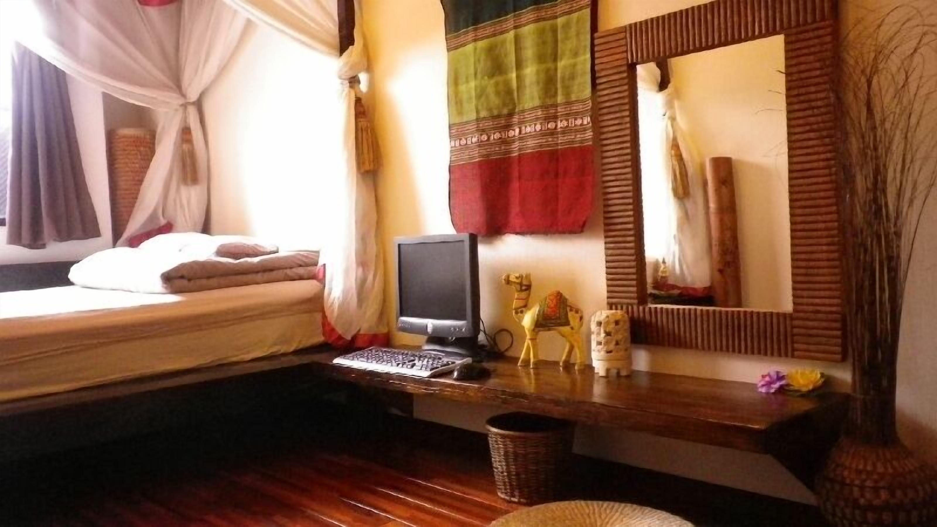 Un dormitorio con cama, un escritorio con computadora, un espejo y objetos decorativos.
