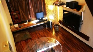 A cozy room with a wooden floor, a glass coffee table, a computer desk, a flat-screen TV, and a fireplace. - Lohas Villa - Hostel (Naha)