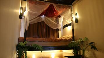 Quarto com cama sob um dossel, mesa de cabeceira e duas luminárias fixadas na parede.