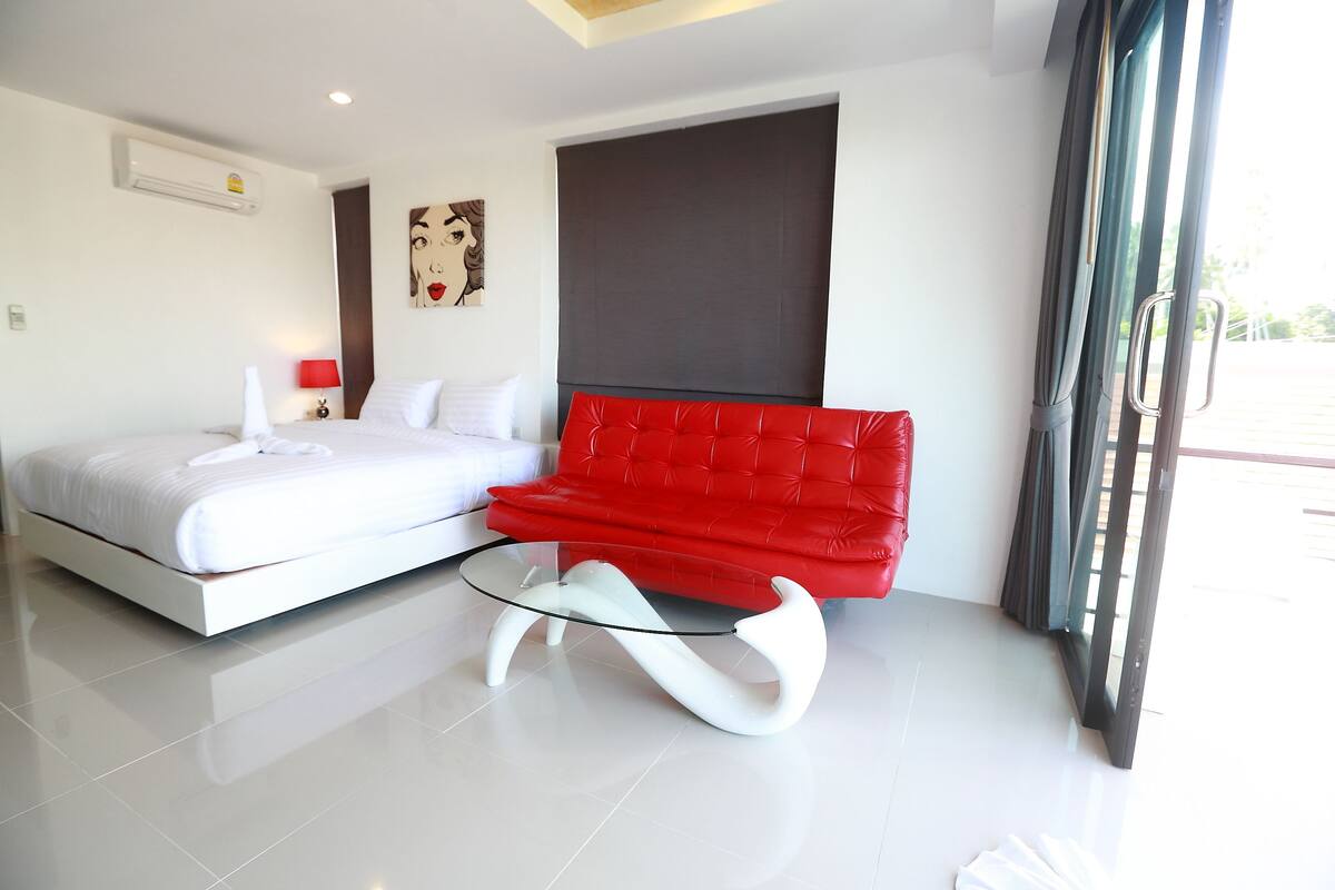 A modern bedroom with a bed, a red sofa, and a glass coffee table.