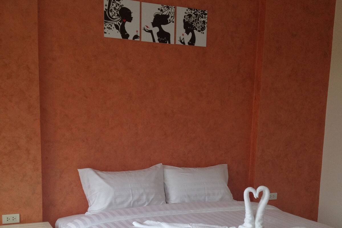 A neatly made bed with white linens and two swan-shaped towels. There is a white nightstand beside the bed, and a wall-mounted artwork above the bed.