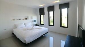 A modern bedroom with a large bed, a nightstand, and three windows with dark blinds. -  Samui Natien Village (Koh Samui)