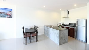 A modern kitchen with a central island, a dining table with chairs, and a refrigerator. -  Samui Natien Village (Koh Samui)