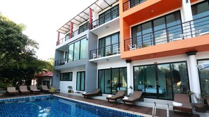 A modern hotel with a swimming pool, multiple balconies, and lounge chairs. -  Samui Natien Village (Koh Samui)