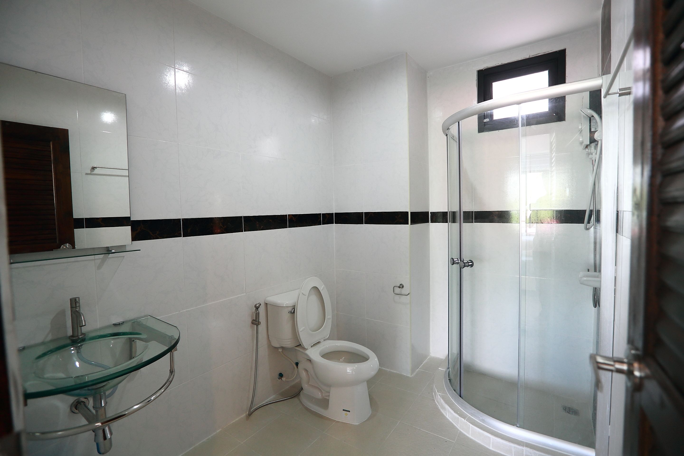 A modern bathroom with a glass sink, a toilet, and a glass-enclosed shower.