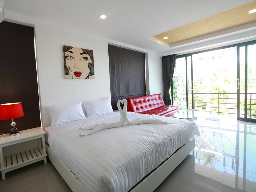 Habitación de hotel con una cama grande, un banco tapizado en rojo, una obra de arte en la pared y vistas al exterior.