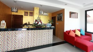 A reception area with a mosaic-tiled counter, a red sofa with colorful cushions, and a large window providing natural light. -  Samui Natien Village (Koh Samui)