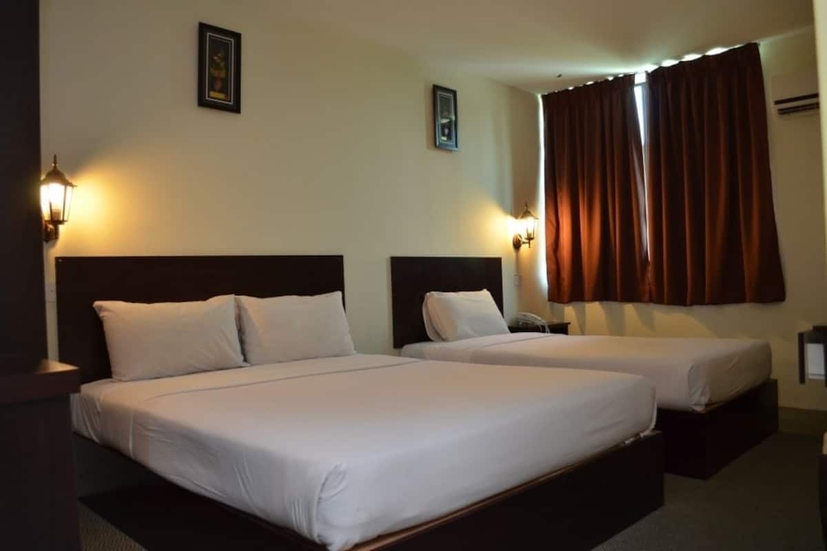 Habitació d'hotel amb dos llits individuals, una finestra gran amb cortines i làmpades subjectes a la paret.