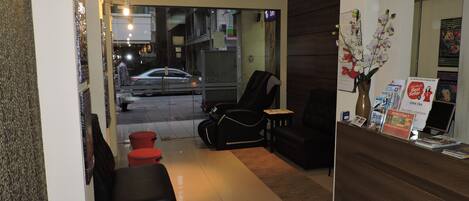 A hotel reception area with a modern design, featuring a reception desk, seating area with red and black chairs, and a vase with flowers.
