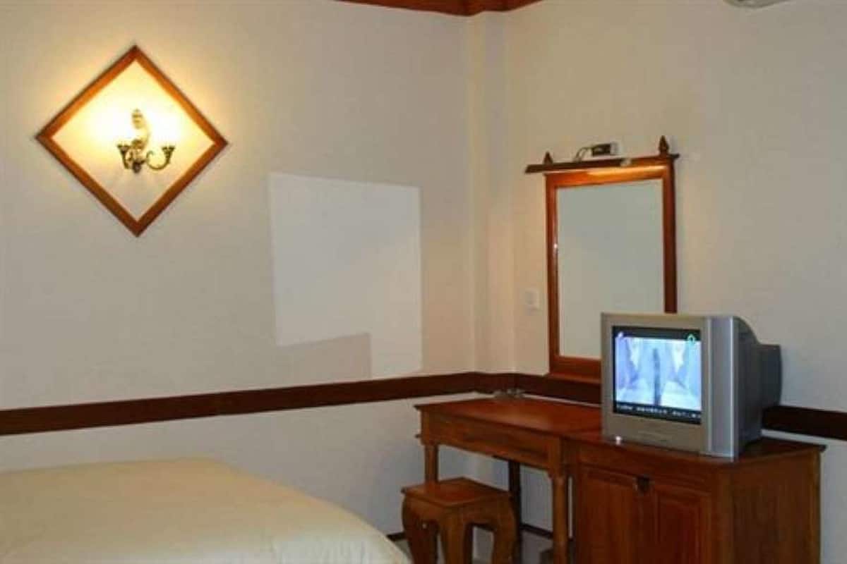 Habitación de hotel con cama, escritorio de madera, televisor, espejo y lámpara de pared.