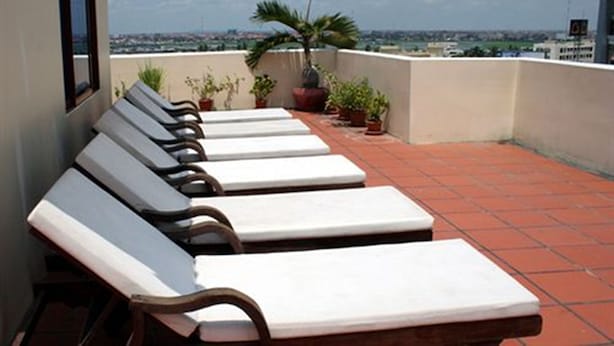 Terraza en la azotea con sillones de sol, plantas en macetas y vistas a la ciudad.