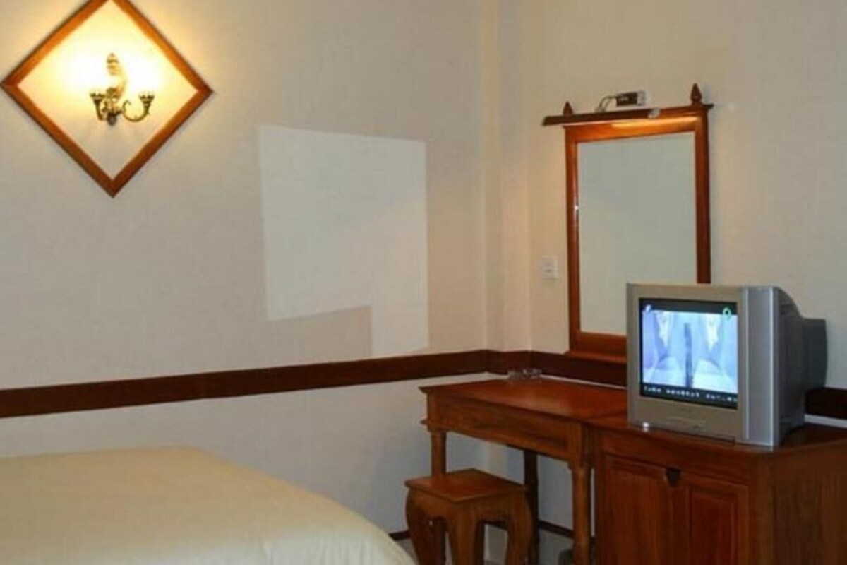 Habitación de hotel con cama, un escritorio de madera con televisor, espejo y lámpara de pared.