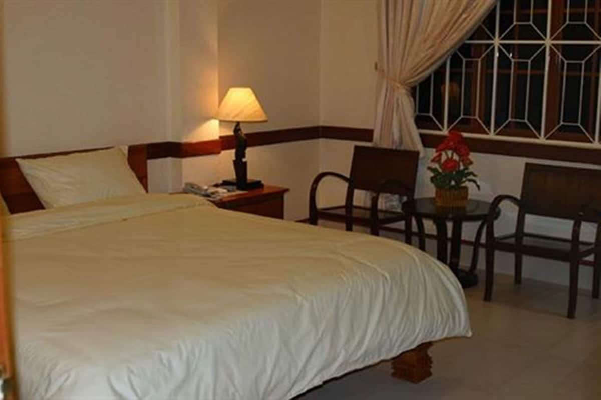 Habitación de hotel con cama, lámpara de noche, silla, mesa y ventana con cortinas.