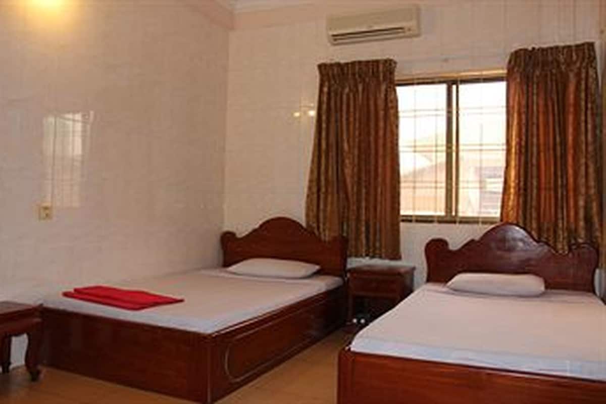 Habitación de hotel con dos camas de madera, una mesita de noche pequeña y una ventana con cortinas.