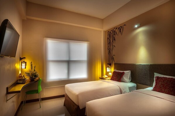 Habitación de hotel con dos camas, un escritorio con silla, televisión y decoración en la pared.