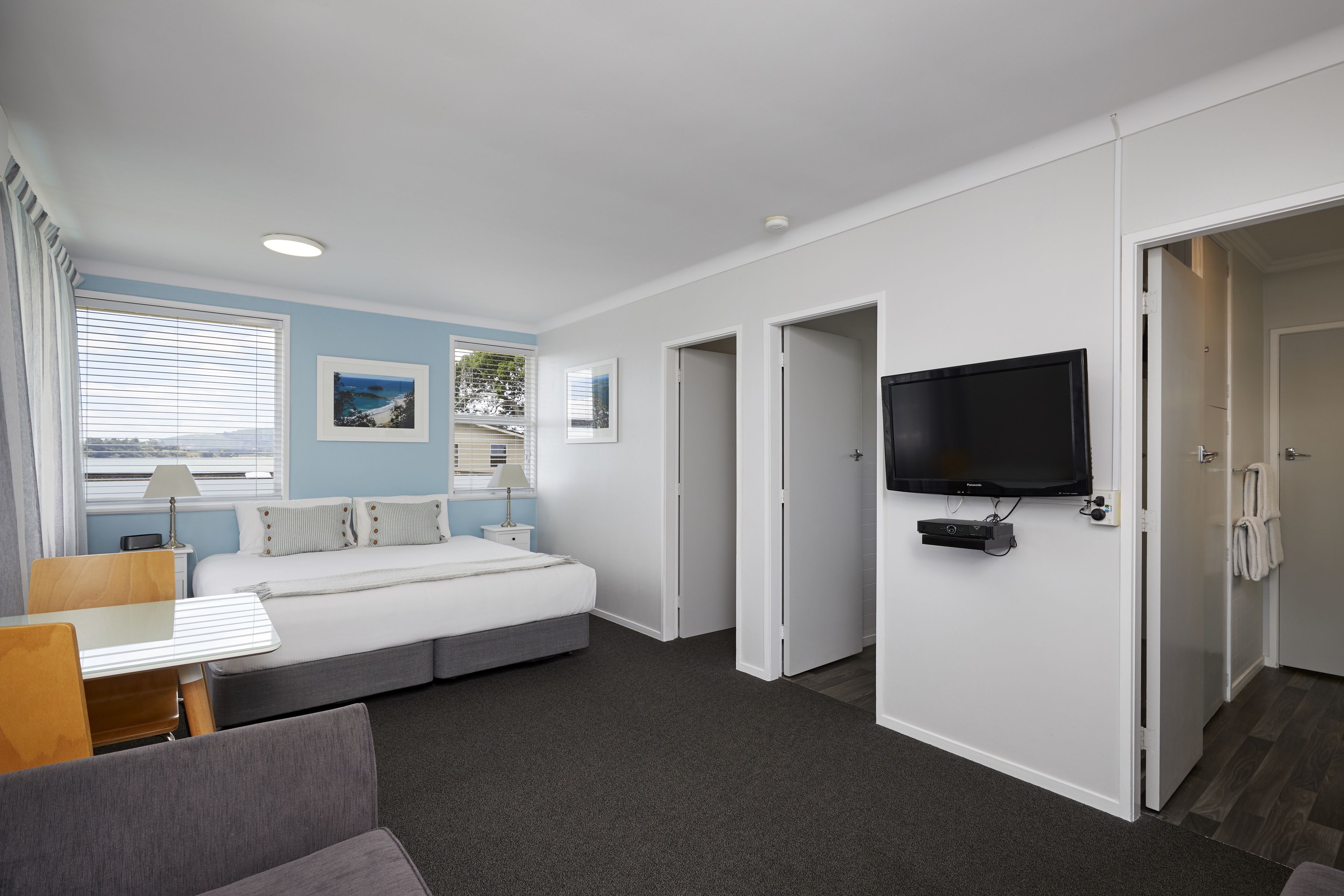Une chambre d’hôtel moderne équipée d’un lit, d’un bureau, d’une télévision et d’une fenêtre avec des stores.