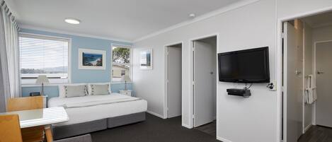 Une chambre d’hôtel moderne équipée d’un lit, d’un bureau, d’une télévision et d’une fenêtre avec des stores.