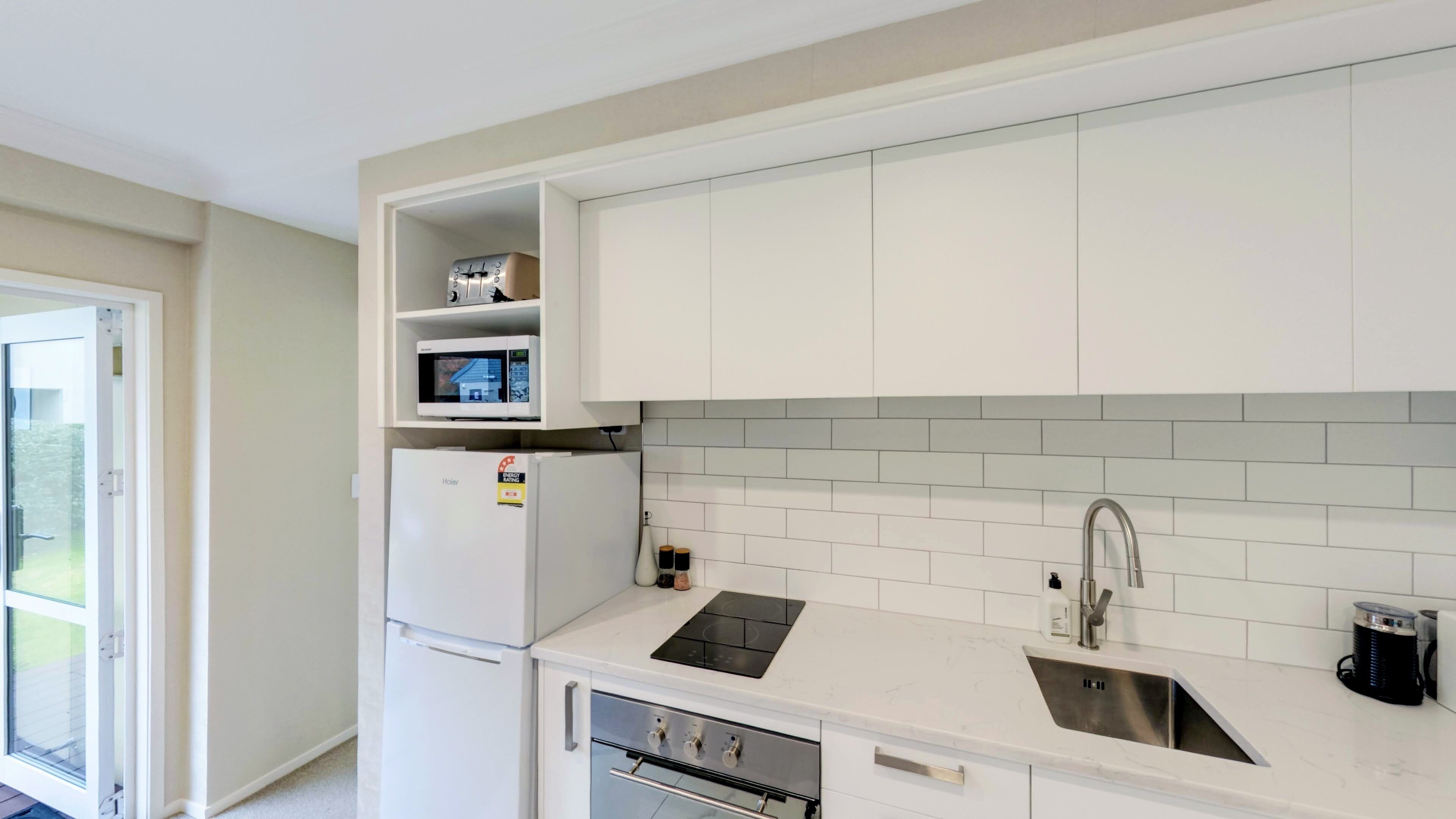 A modern kitchen with white cabinets, a built-in microwave, a refrigerator, a sink, and a stove.