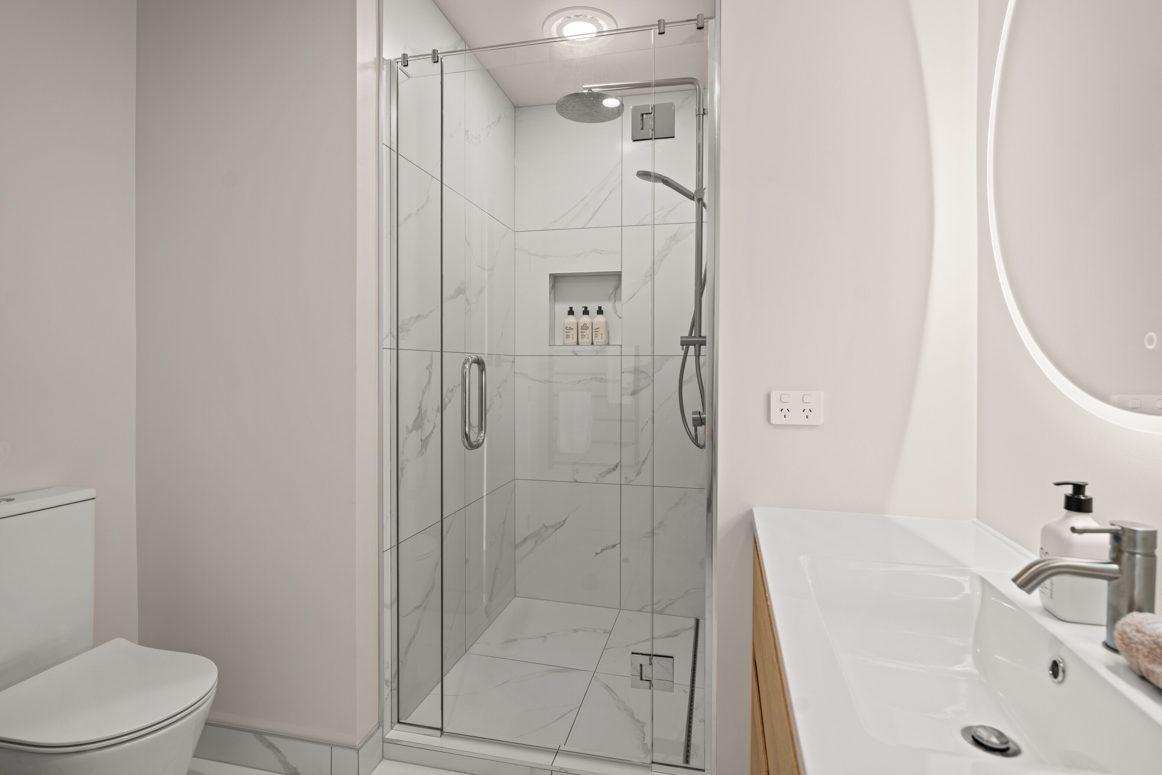 A modern bathroom with a glass-enclosed shower, a white toilet, and a sink with a mirror.