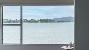 A room with a large window overlooking a body of water and distant hills. - Harbour View Motel and Water Front Apartments (Tauranga)