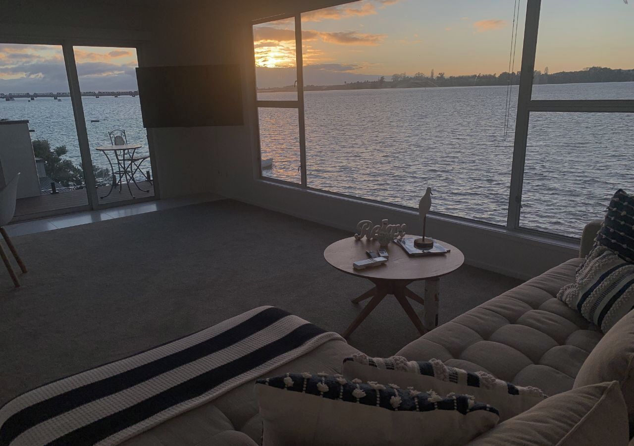 A living room with a large window overlooking a body of water, a sofa, a small round table, and a chair.