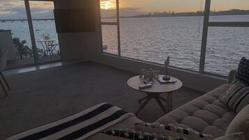 A living room with a large window overlooking a body of water, a sofa, a small round table, and a chair.