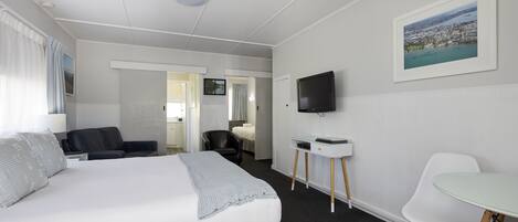 Een hotelkamer met een bed, een bureau, een stoel, een televisie en een ingelijst kunstwerk aan de muur.