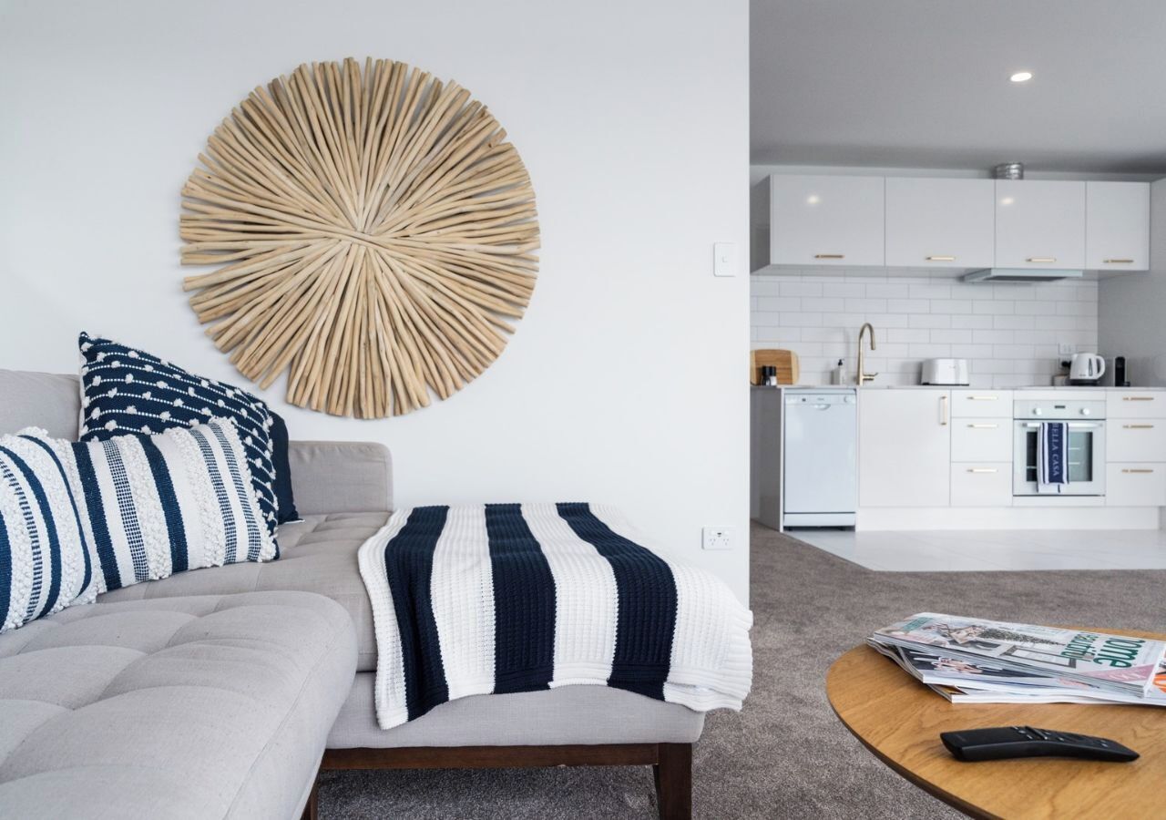 A modern living room with a grey sofa, striped pillows, and a round wall decoration. A coffee table with a remote control and magazines is in the foreground.