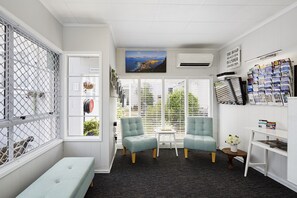 Ein Zimmer mit Meerblick, eine Bank, zwei Sessel, ein kleiner Tisch und eine Wand mit gerahmten Bildern und einem motivierenden Zitat.