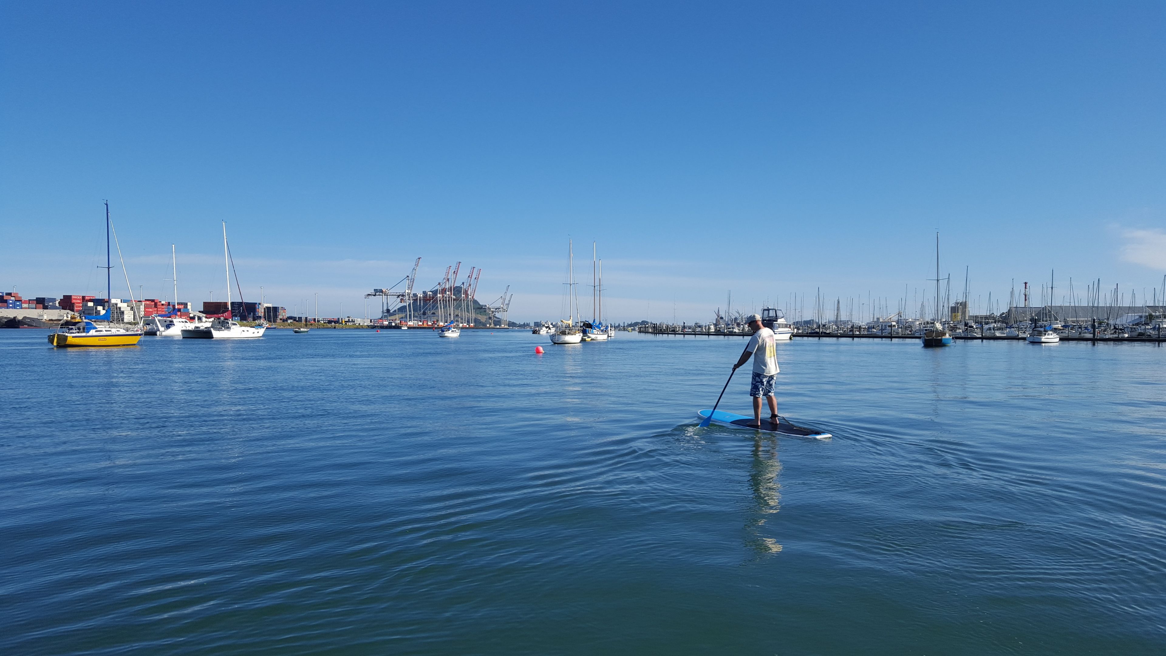 Una marina con diverse imbarcazioni e una persona che fa paddleboarding.