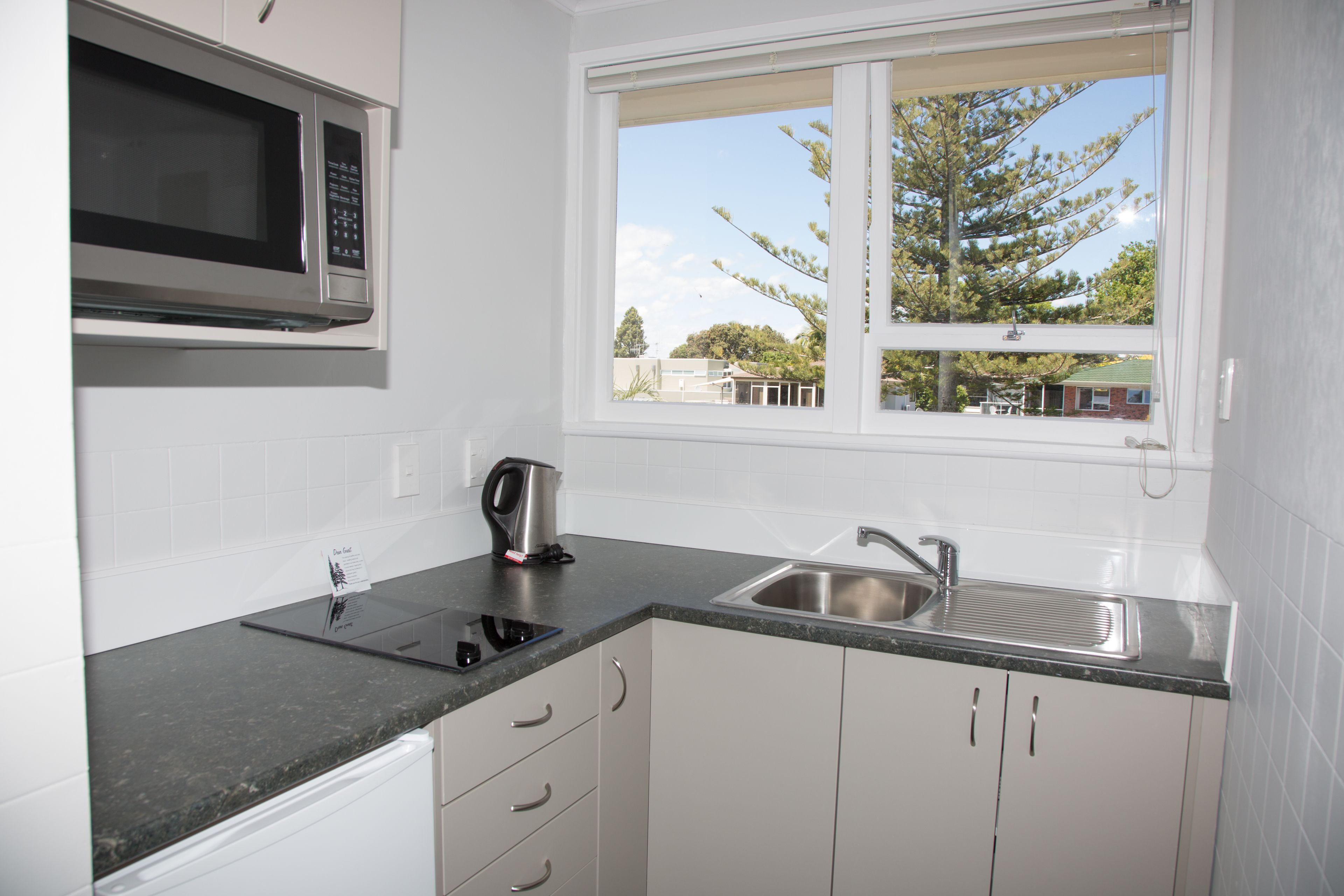 A modern kitchen with white cabinets, a stainless steel sink, a microwave, and a kettle.