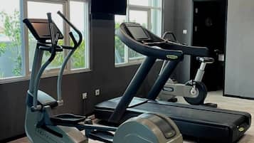 A gym with cardio machines, large windows, and a door.