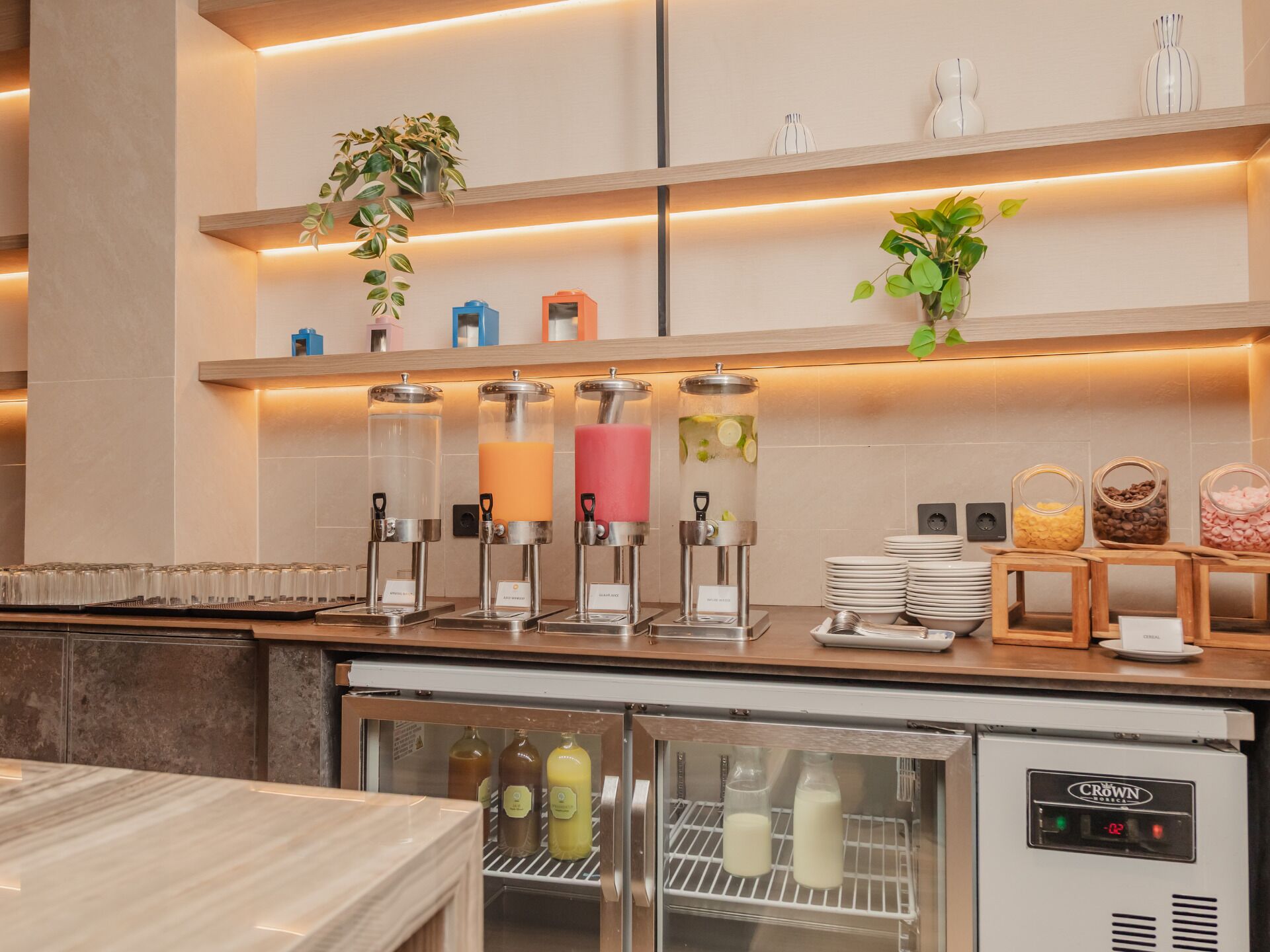 A breakfast bar with a coffee machine, juice dispensers, and a refrigerator with milk bottles.