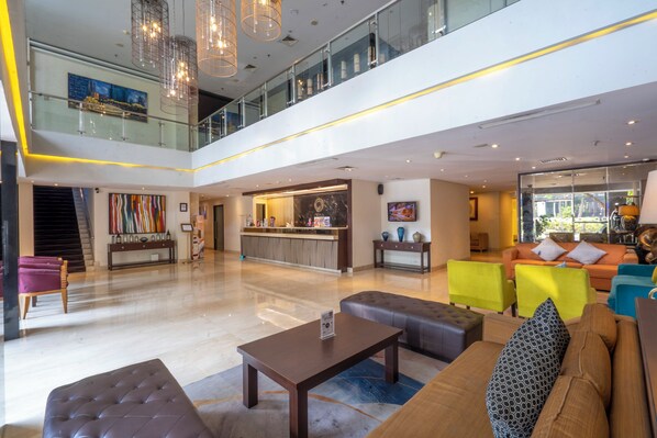 A spacious lobby with a high ceiling, a central seating area with sofas and chairs, a reception desk, and a staircase leading to an upper level. - Oria Hotel Jakarta (Jakarta)