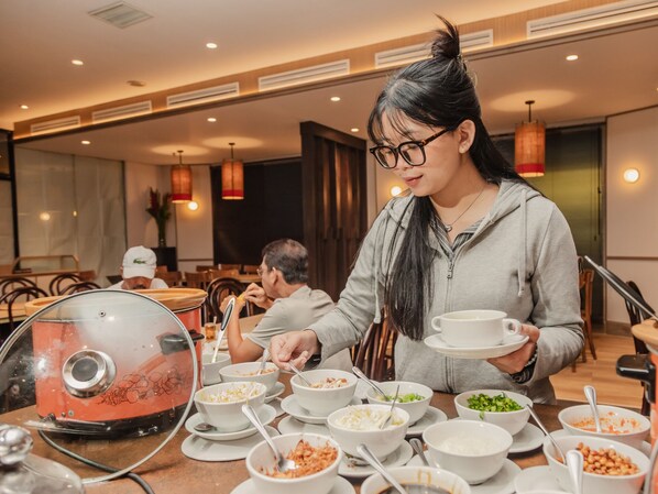 A dining area with multiple tables, some with bowls of food and a steam kettle. - Oria Hotel Jakarta (Jakarta)