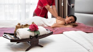 A massage therapy session in a room with a bed, a massage table, and a tray with towels and a rose. - Oria Hotel Jakarta (Jakarta)