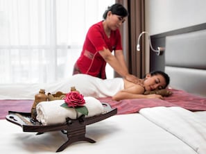 A massage therapy session in a room with a bed, a massage table, and a tray with towels and a rose. - Oria Hotel Jakarta (Jakarta)