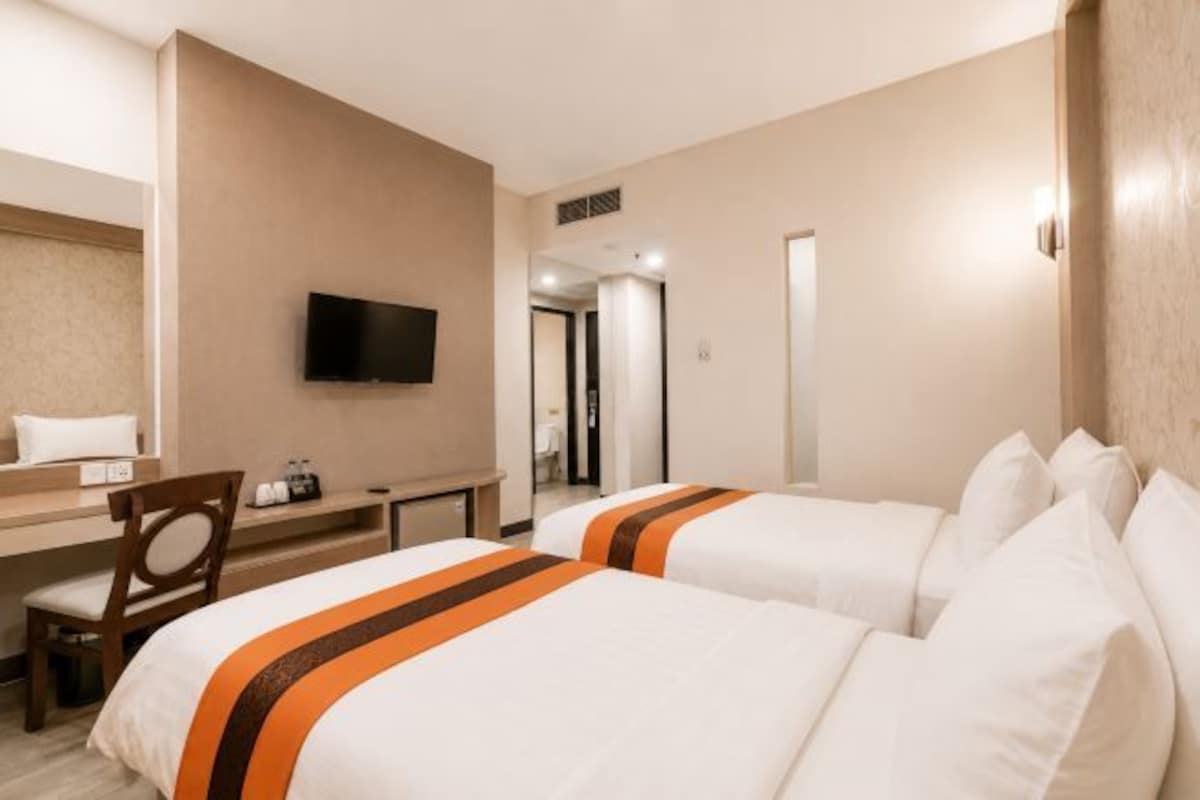 A hotel room with two beds, a desk, a chair, a television, and a door leading to another room.
