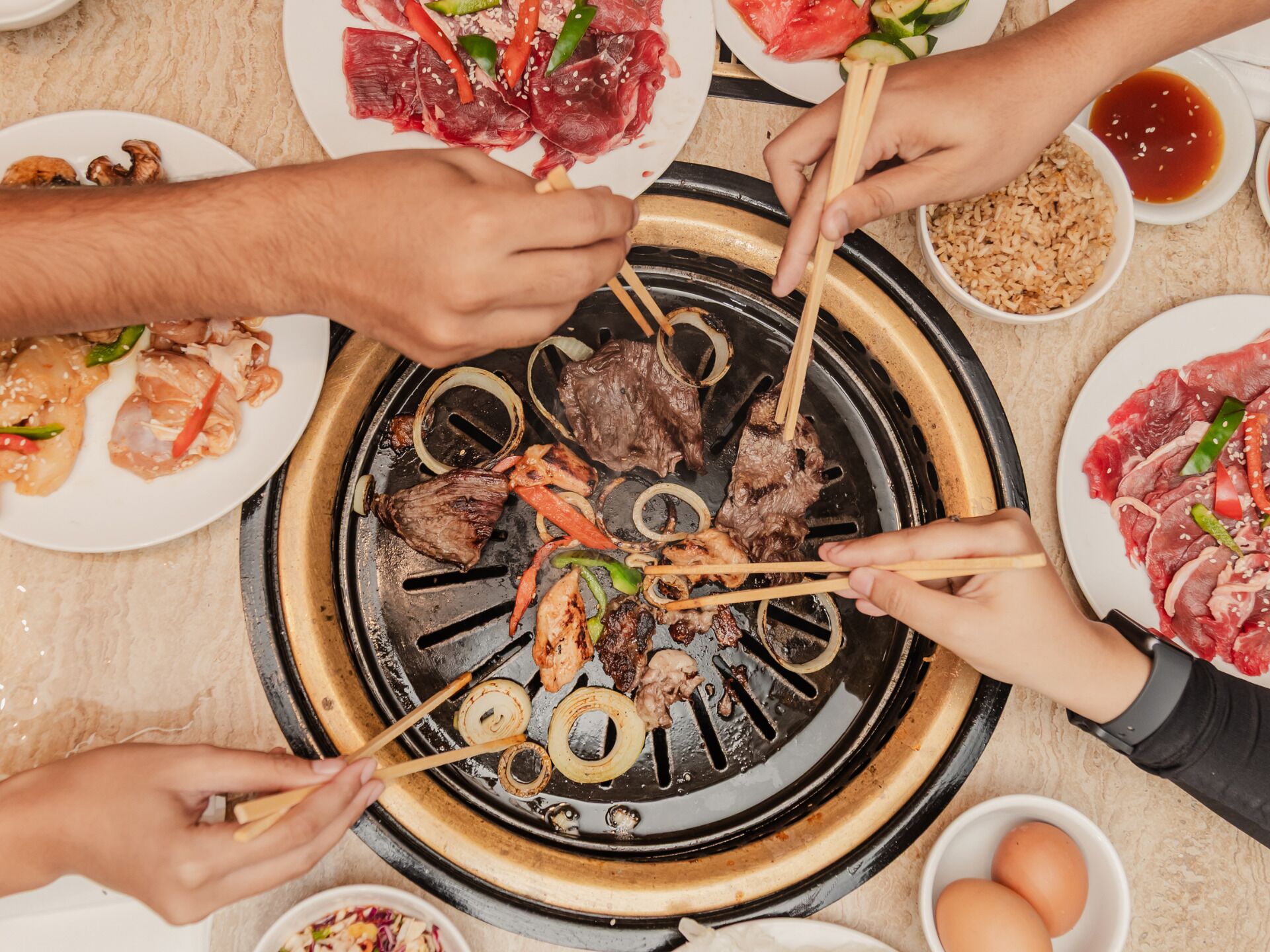 A group of people cooking various meats on a grill.
