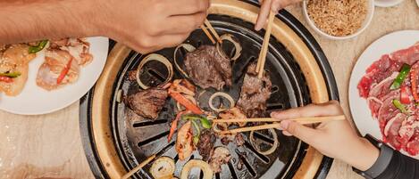 A group of people cooking various meats on a grill.