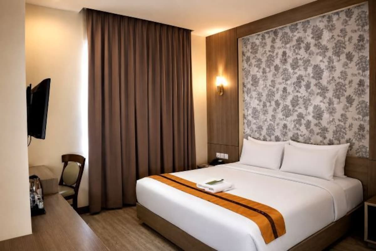 A hotel room with a bed, a desk, a chair, a TV, and a window with curtains.