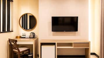 Habitación de hotel con escritorio, silla, televisor y un mueble pequeño.