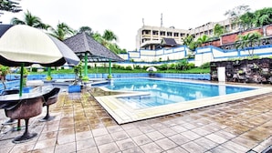 A swimming pool with a tiled deck, a covered seating area, and a building in the background. - Sahid Manado (Manado)