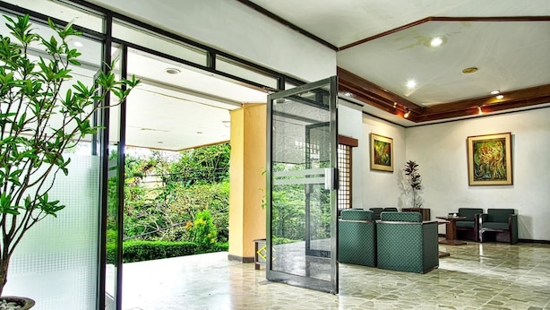 A reception area with a glass door leading to a garden, a seating area with green upholstered chairs, and a tiled floor. - Sahid Manado (Manado)