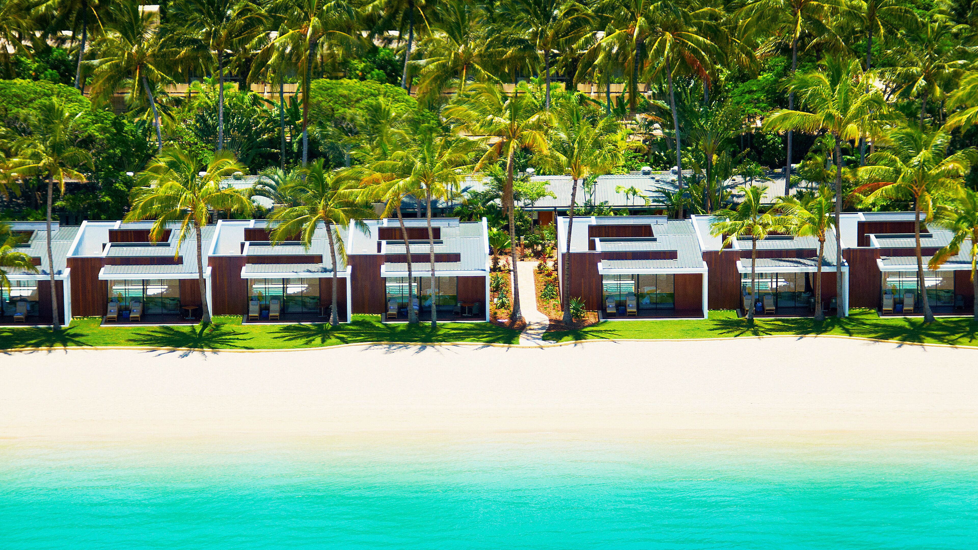 A beachfront resort with modern villas, palm trees, and a clear view of the turquoise ocean.