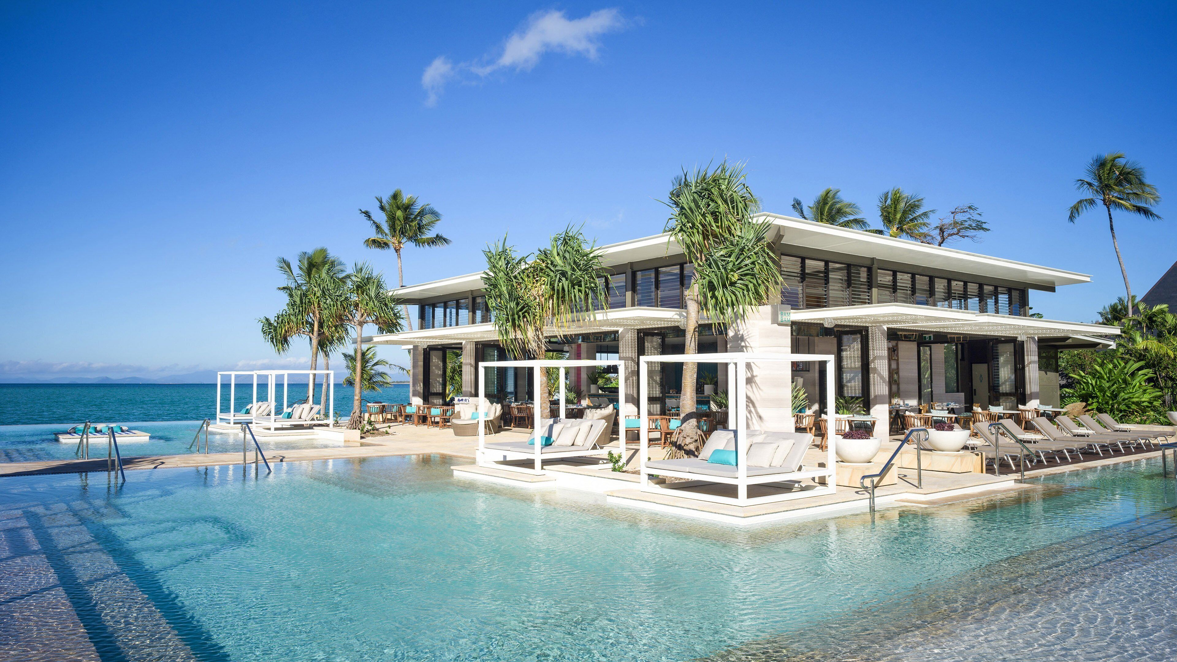 A modern resort with a pool, lounge areas, and a view of the ocean.