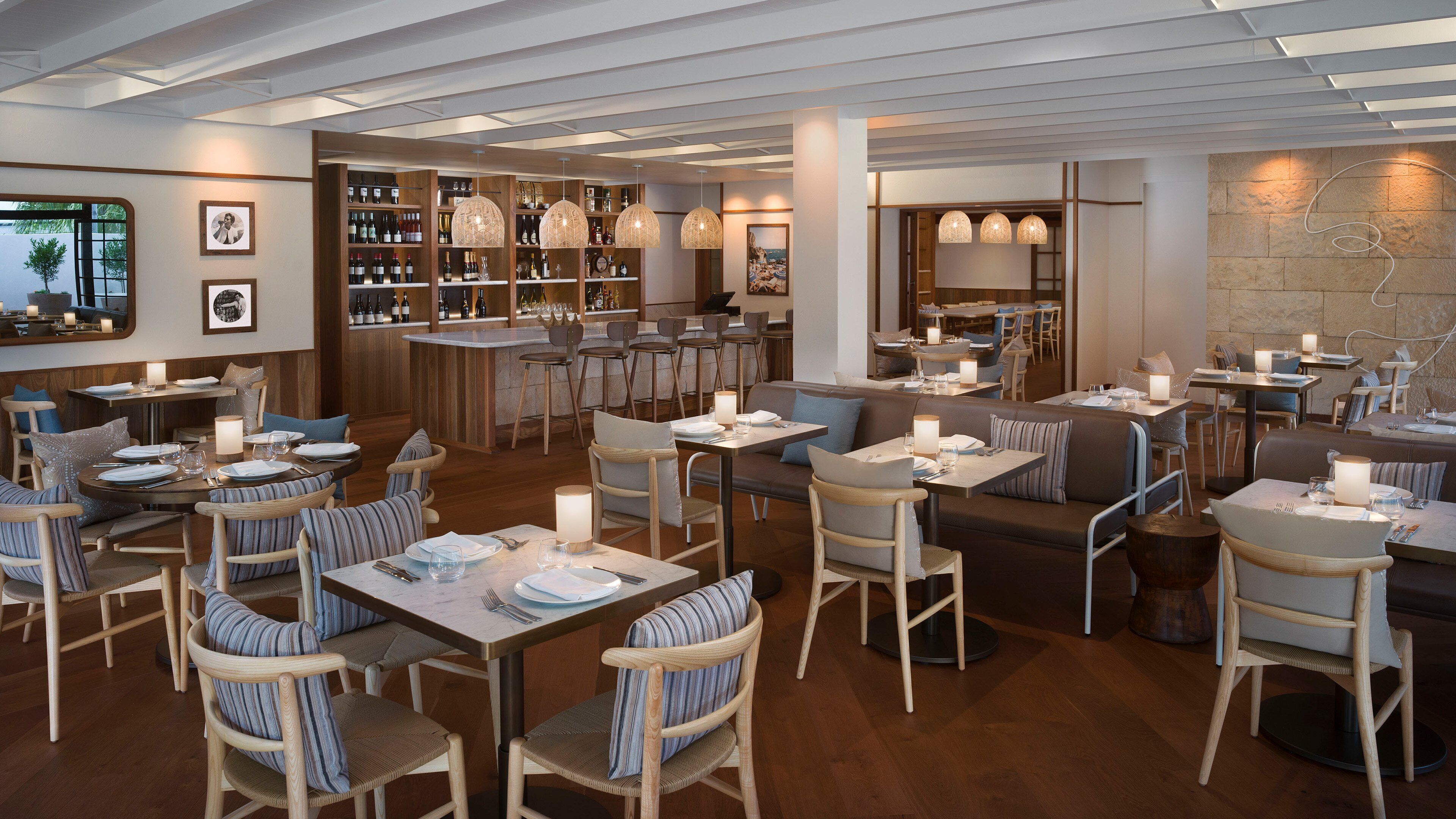 Un restaurante con mobiliario de madera, una zona de bar y lámparas colgantes.
