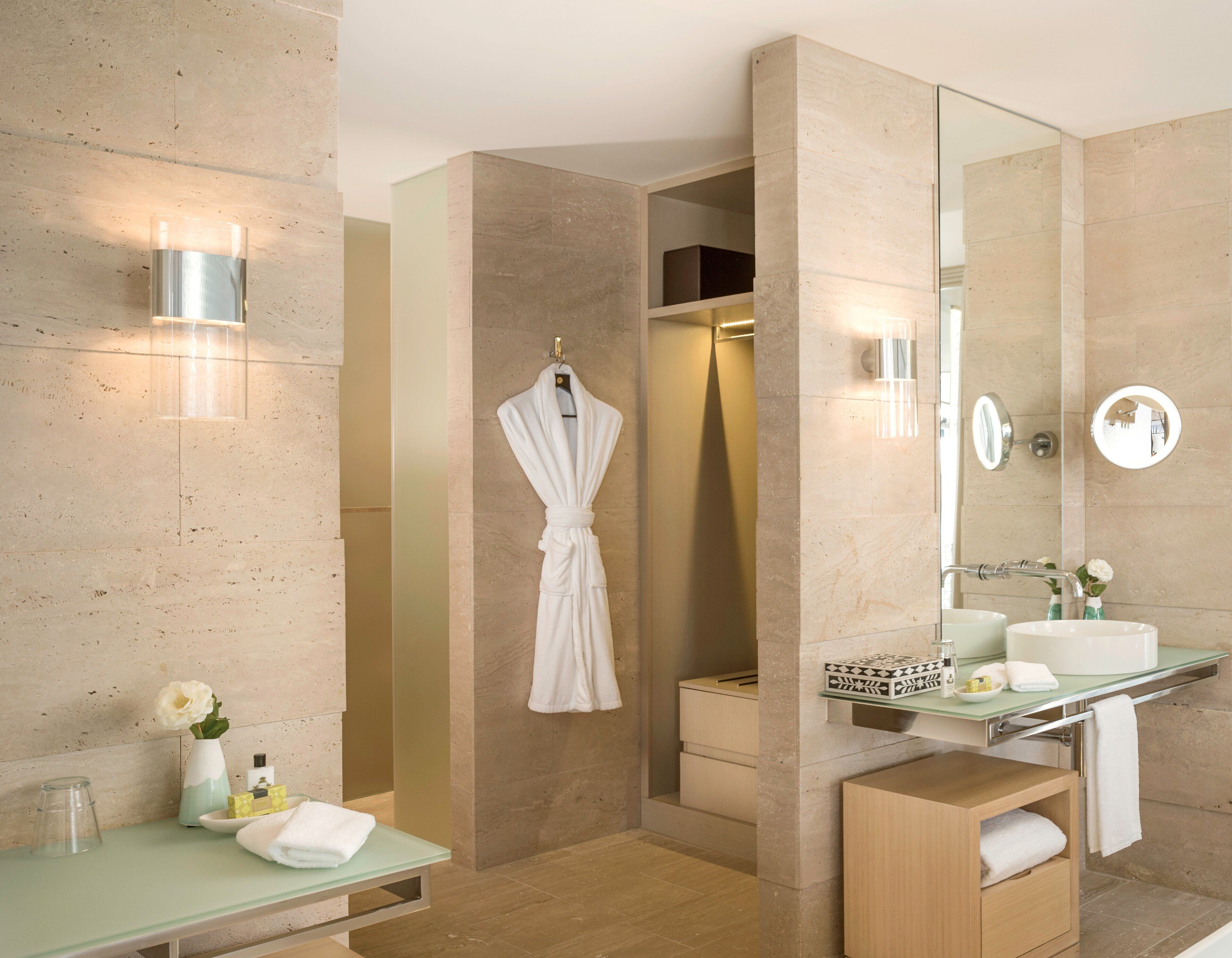 A modern bathroom with a glass vanity, a large mirror, a robe hanging on a hook, and a shower area.