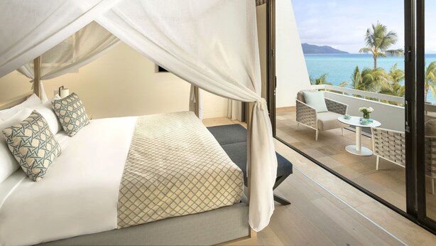 A bedroom with a canopy bed, a balcony with outdoor seating, and a view of the ocean. - InterContinental Hayman Great Barrier Reef by IHG (Whitsundays)