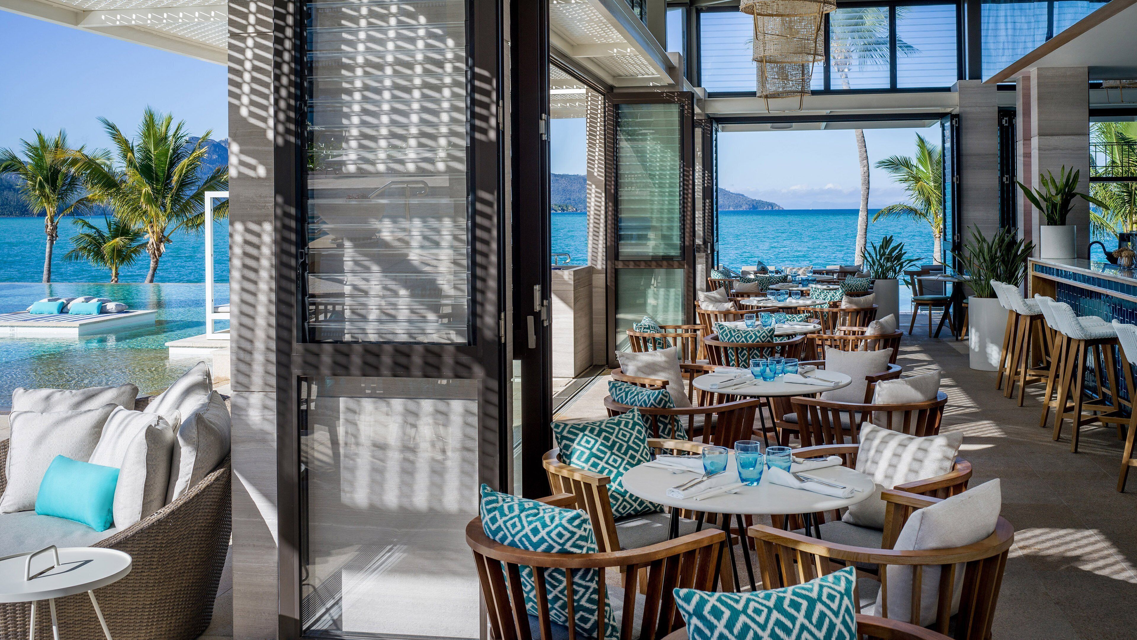 A seaside restaurant with outdoor seating, a pool, and a view of the ocean.